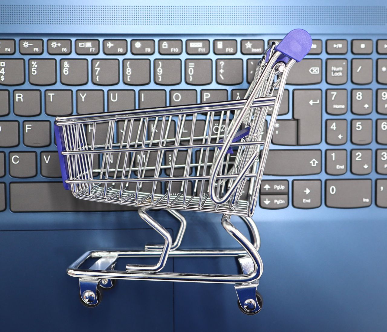 about-02 A miniature shopping cart placed on a laptop keyboard symbolizing online shopping and e-commerce.