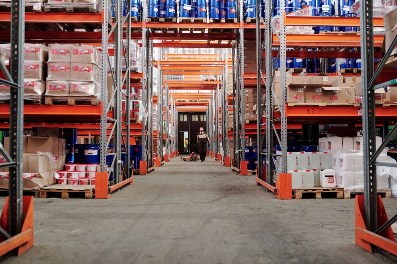 services-img A spacious industrial warehouse with stocked shelves and a worker in protective gear.
